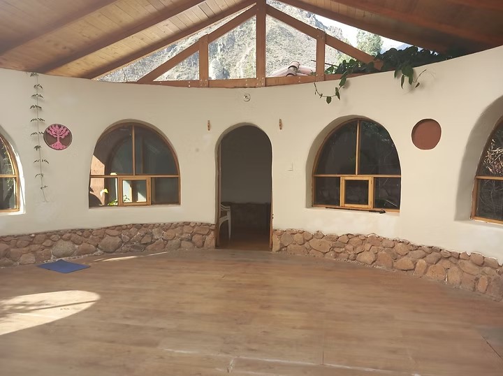 A round room with a wooden floor, arched windows and a timber roof open to the mountains