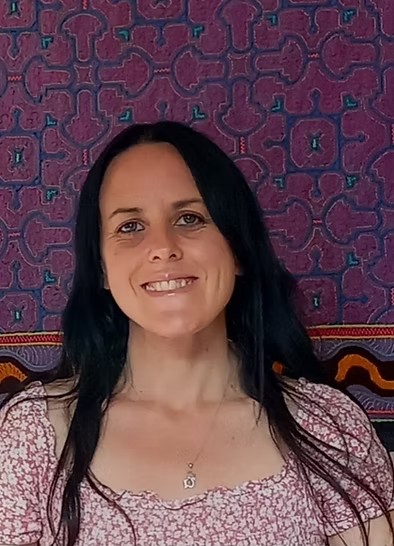 A smiling woman with long dark hair in front of a patterned textile