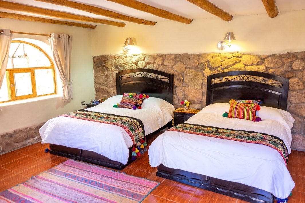 A bedroom with two beds under woven runners, a stone wall and an arched window