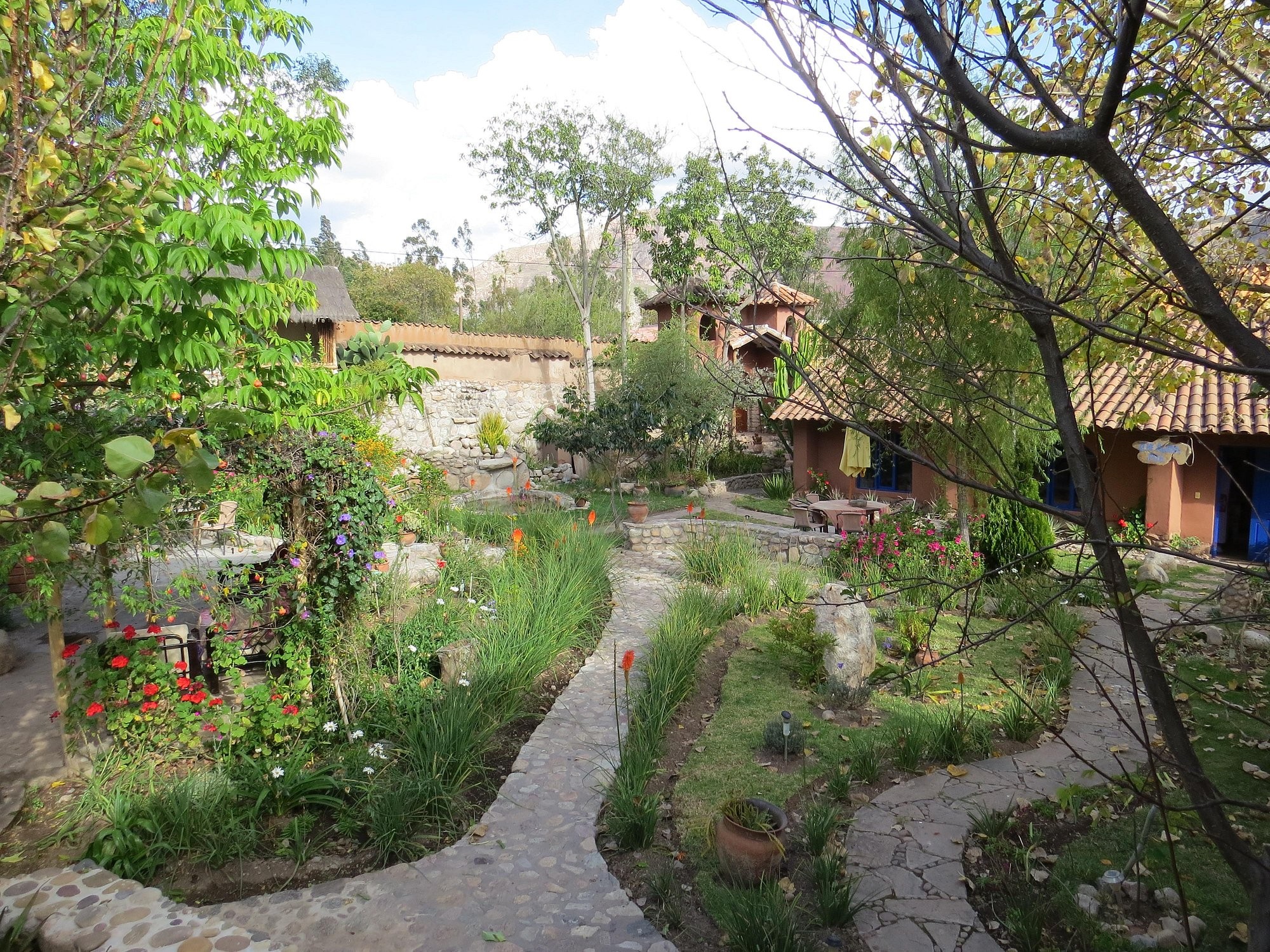 Stone paths winding through a flower garden toward adobe buildings