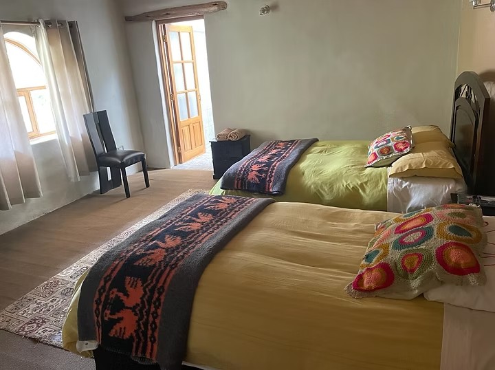 A bedroom with two beds under woven blankets and a door open to the light