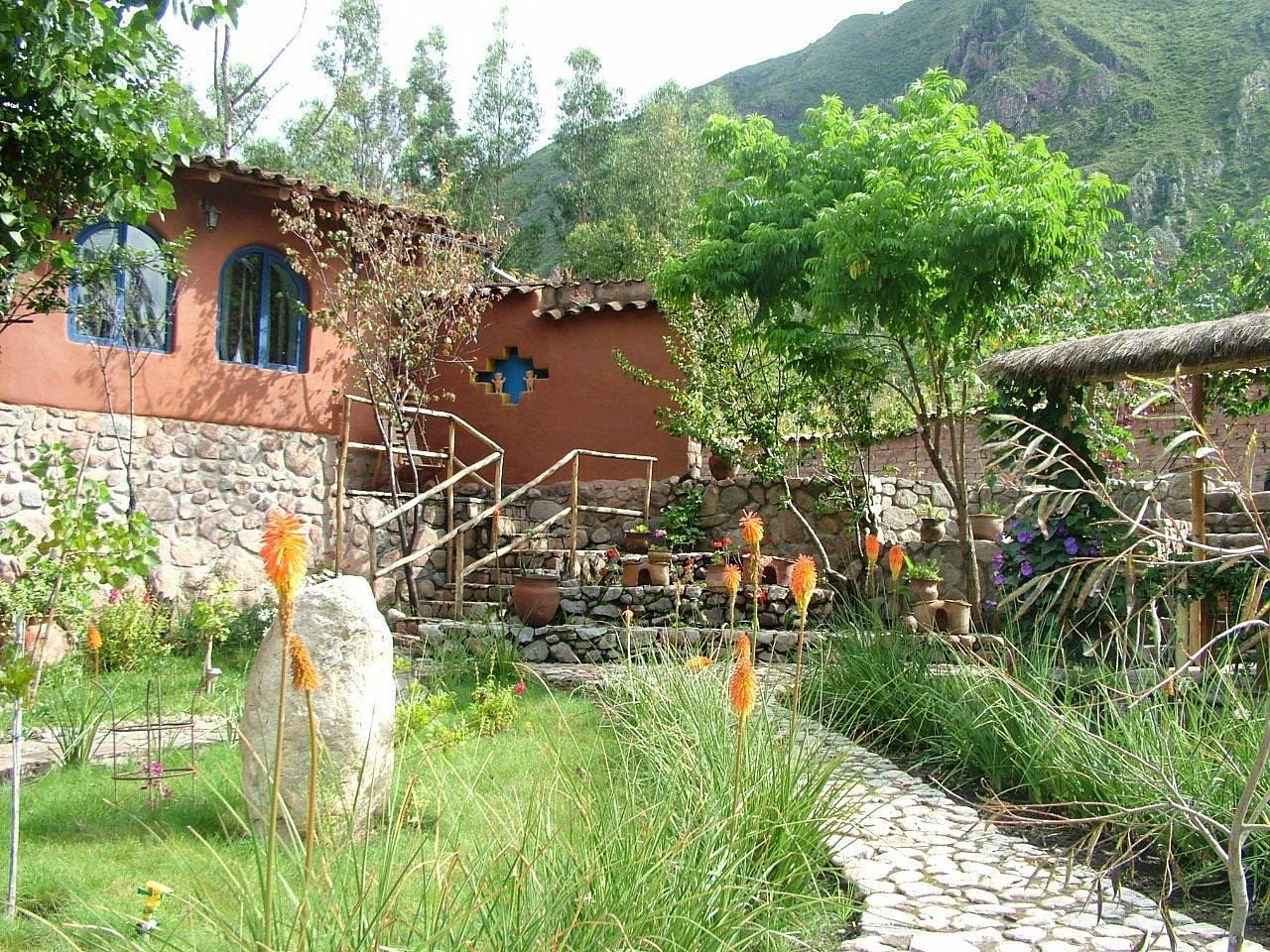 La Capilla Lodge, a terracotta building above a garden of orange flowers and a stone path, green mountains behind