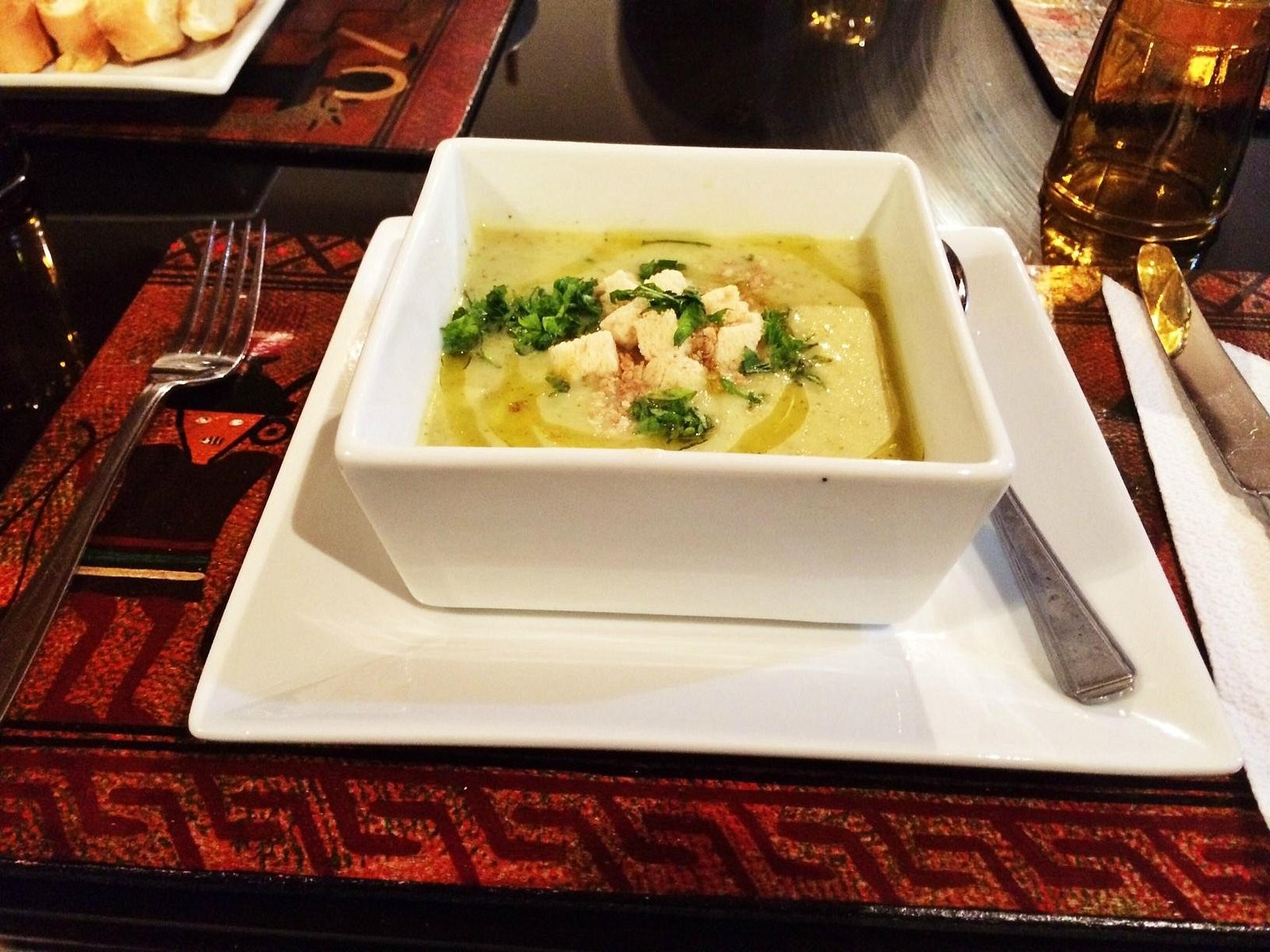 A bowl of soup at La Capilla Lodge, on a square white plate and a red woven place mat