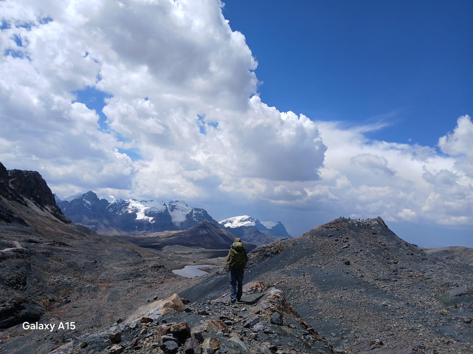A hiker on a rocky ridge below snowy peaks and a sky of white cloud